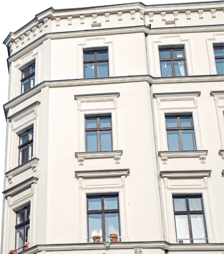 Fassade eines Altbaus mit weißen Wänden und mehreren Fenstern im klassischen Stil, die symmetrisch angeordnet sind.