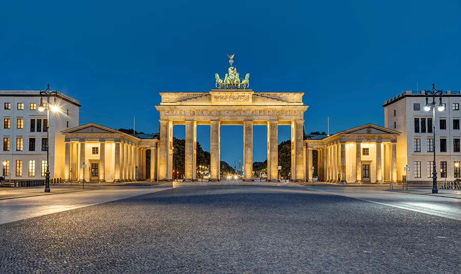Das Brandenburger Tor in Berlin bei Nacht, beleuchtet und umgeben von leeren Straßen und Gebäuden im Hintergrund.
